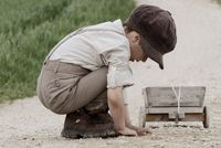 Kleiner Junge mit Schiebermütze und Holzwagen auf einem Feldweg