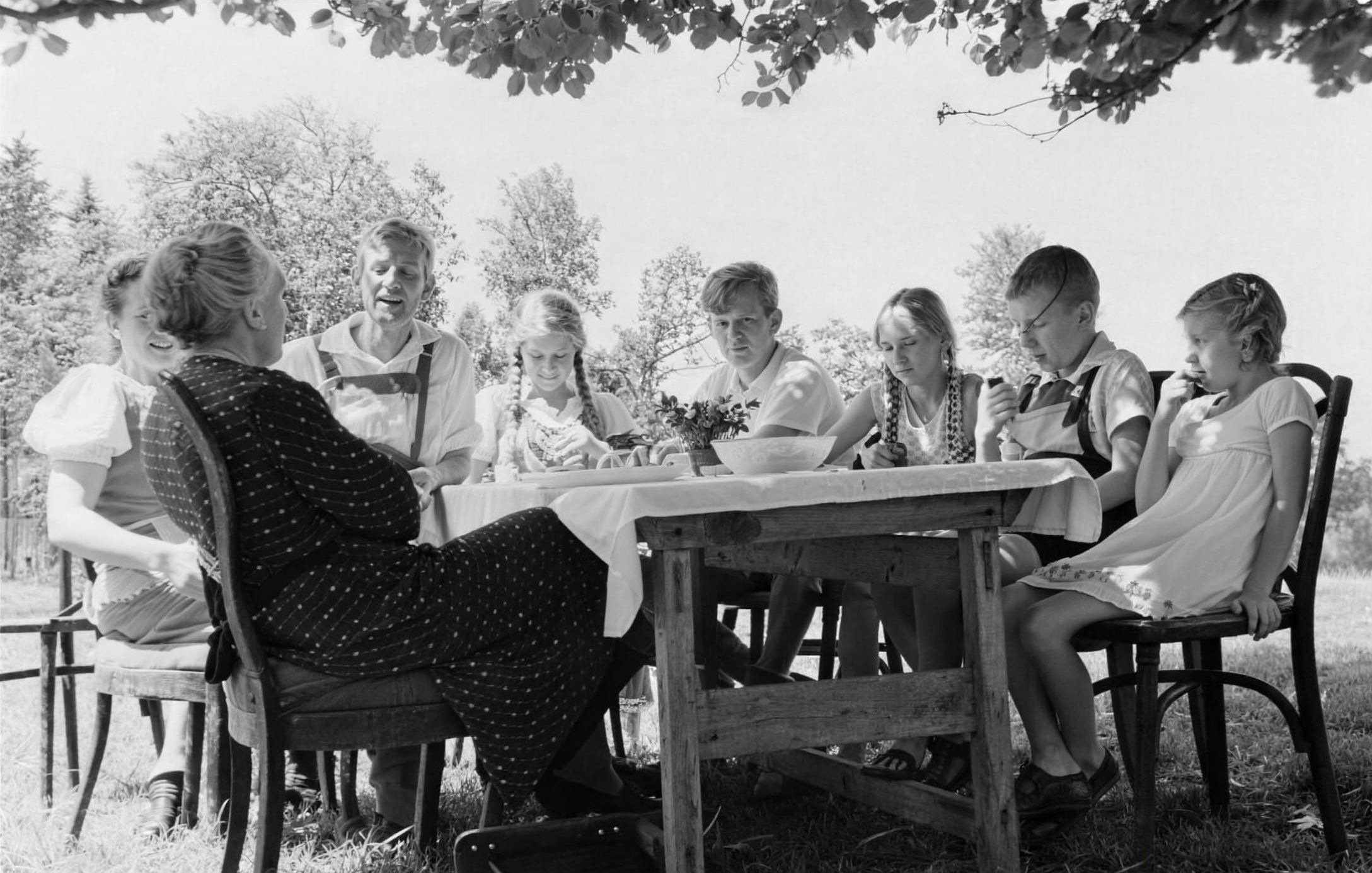 Historisches Schwarz-Weiß-Foto: Großfamilie mit Kindern an einem gedeckten Tisch im Freien unter Bäumen