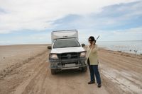 Frau mit Funkgerät neben einem Geländewagen auf einer Sandpiste