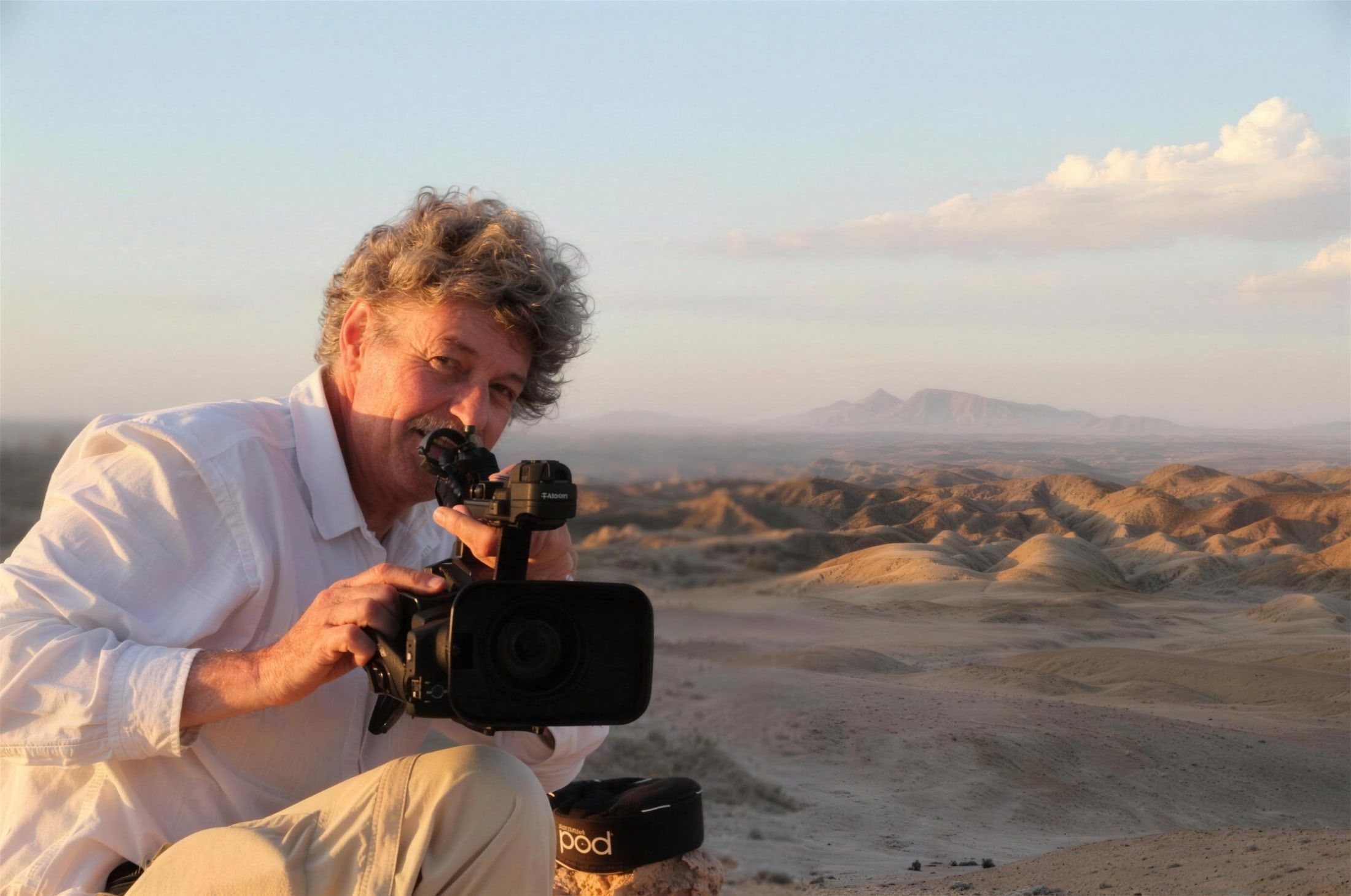 Rüdiger Lorenz mit Videokamera in einer kargen Berg- und Wüstenlandschaft im Abendlicht